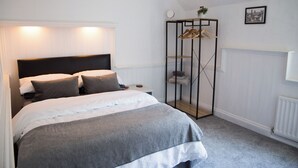 Une chambre à coucher comprenant un lit, une table de chevet, un porte-vêtements suspendu et un radiateur.