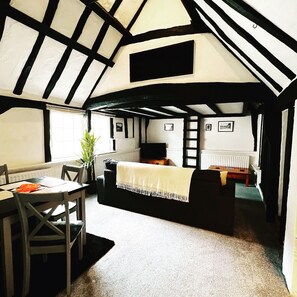A room with a high ceiling, exposed beams, a bed, a table with chairs, and a radiator.