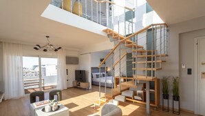 A modern apartment with a wooden staircase, a balcony with a view, a dining area, and a living room with a sofa and a TV. - Acropolis Sky Retreat Jacuzzi 3BR Maisonette (Athens)