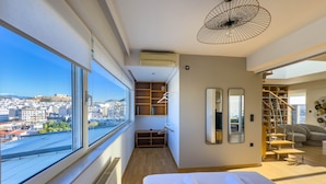 A modern hotel room with a large window offering a city view, a neatly made bed, a walk-in closet, and a staircase leading to an upper level. - Acropolis Sky Retreat Jacuzzi 3BR Maisonette (Athens)