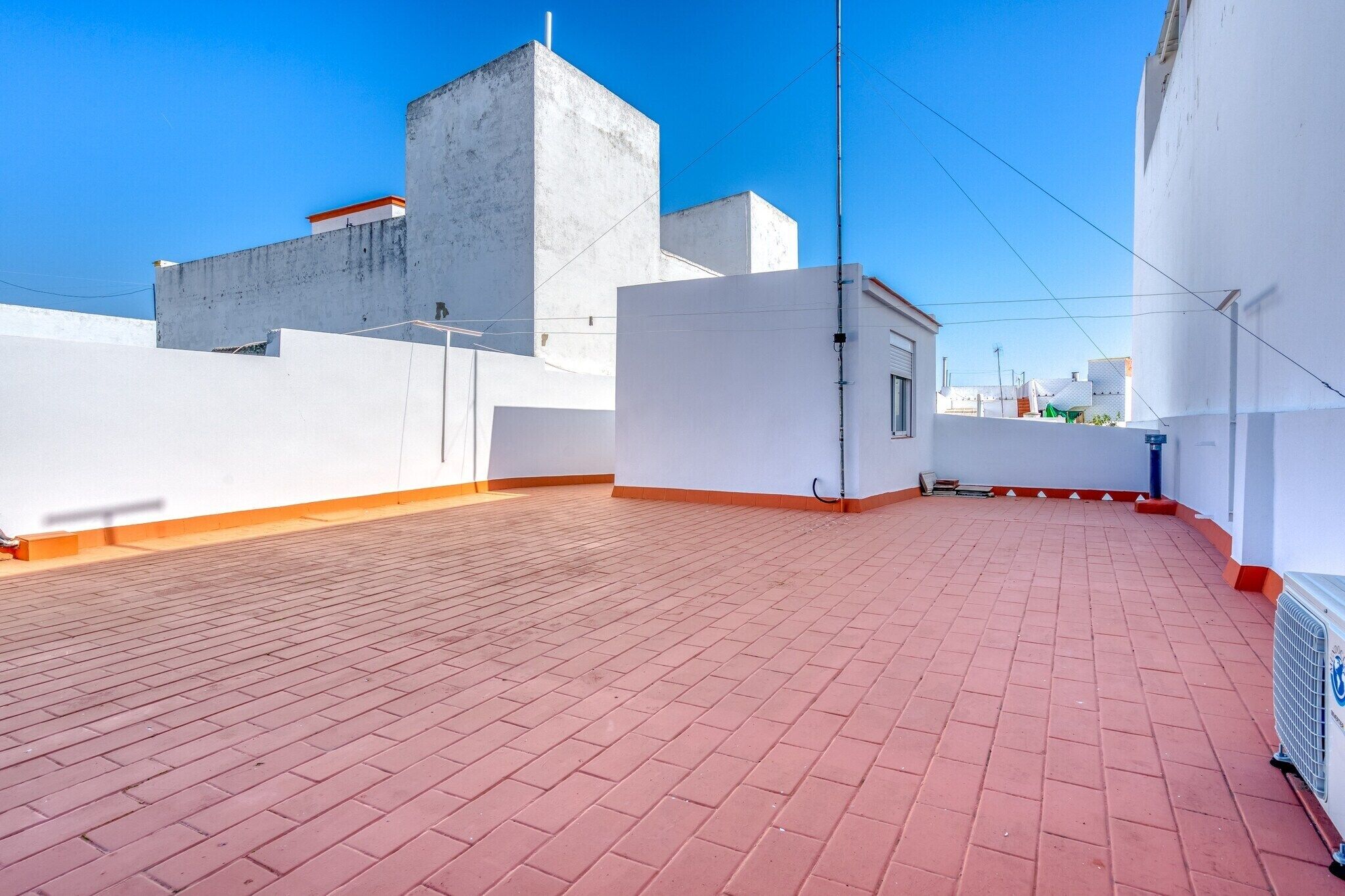 A rooftop terrace with red tiles, white walls, and a concrete structure.