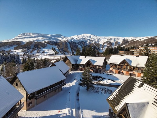 A snow-covered lodge with multiple wooden cabins, a ski lift, and a mountainous backdrop. - Two quiet rooms with pool in Super-Besse (Besse-et-Saint-Anastaise-Super Besse)
