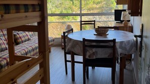 Habitació acollidora amb un llit superposat, una taula rodona amb seients i vista a un vessant boscós.