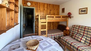 Habitació acollidora amb un llit superposat, un sofà escocès, una taula petita amb un cistell i prestatgeries de fusta decorades amb objectes ornamentals.