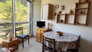 Una habitació acollidora amb taula de menjador, cadirees, televisió i finestra amb vista al bosc.