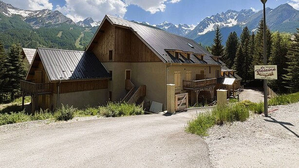 En rustik fjeldhytte med metal tag, træfacade og et skilt med teksten 'La Residence'.
