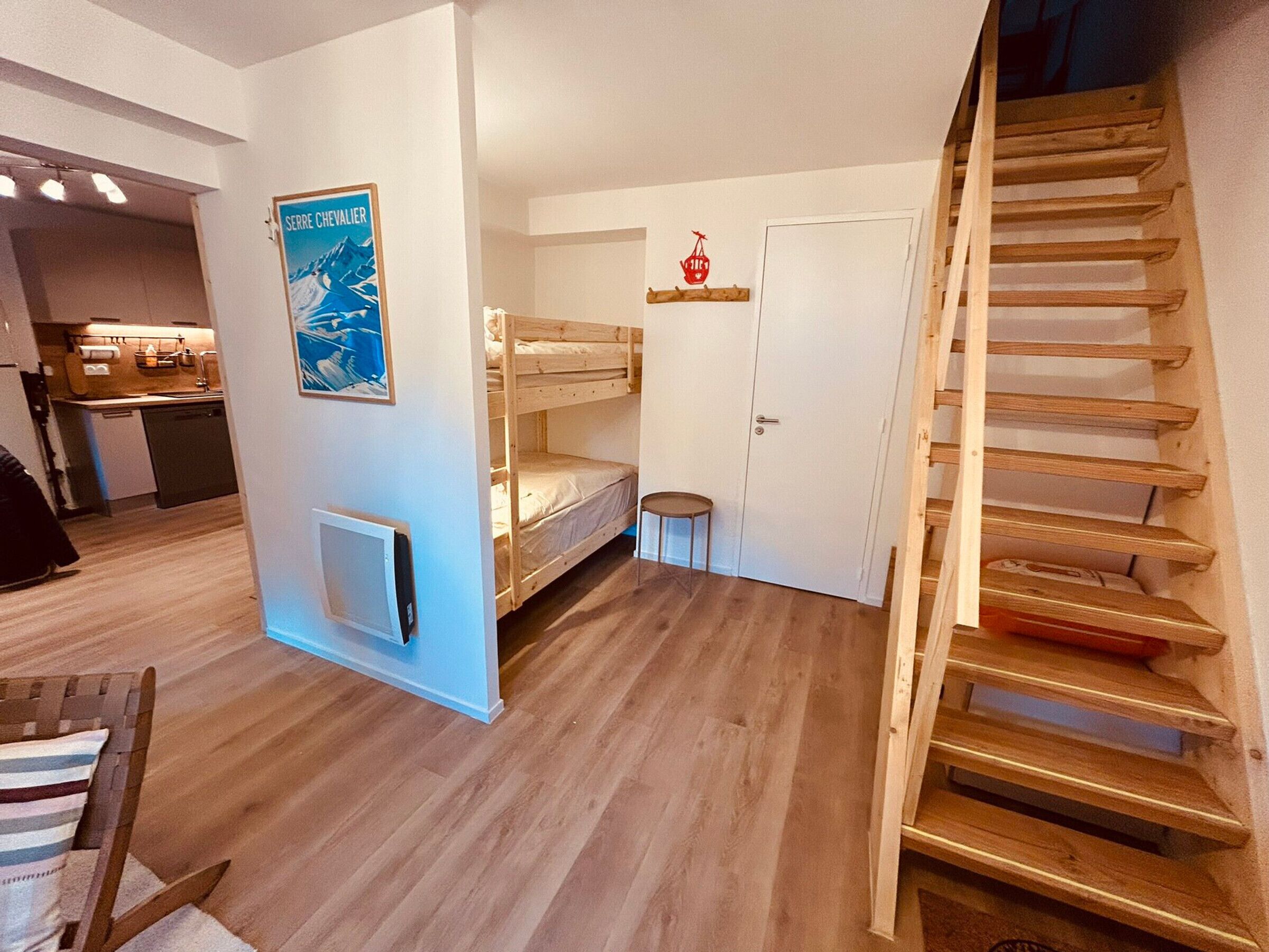 A compact room with bunk beds, a small stool, a door, and a staircase.