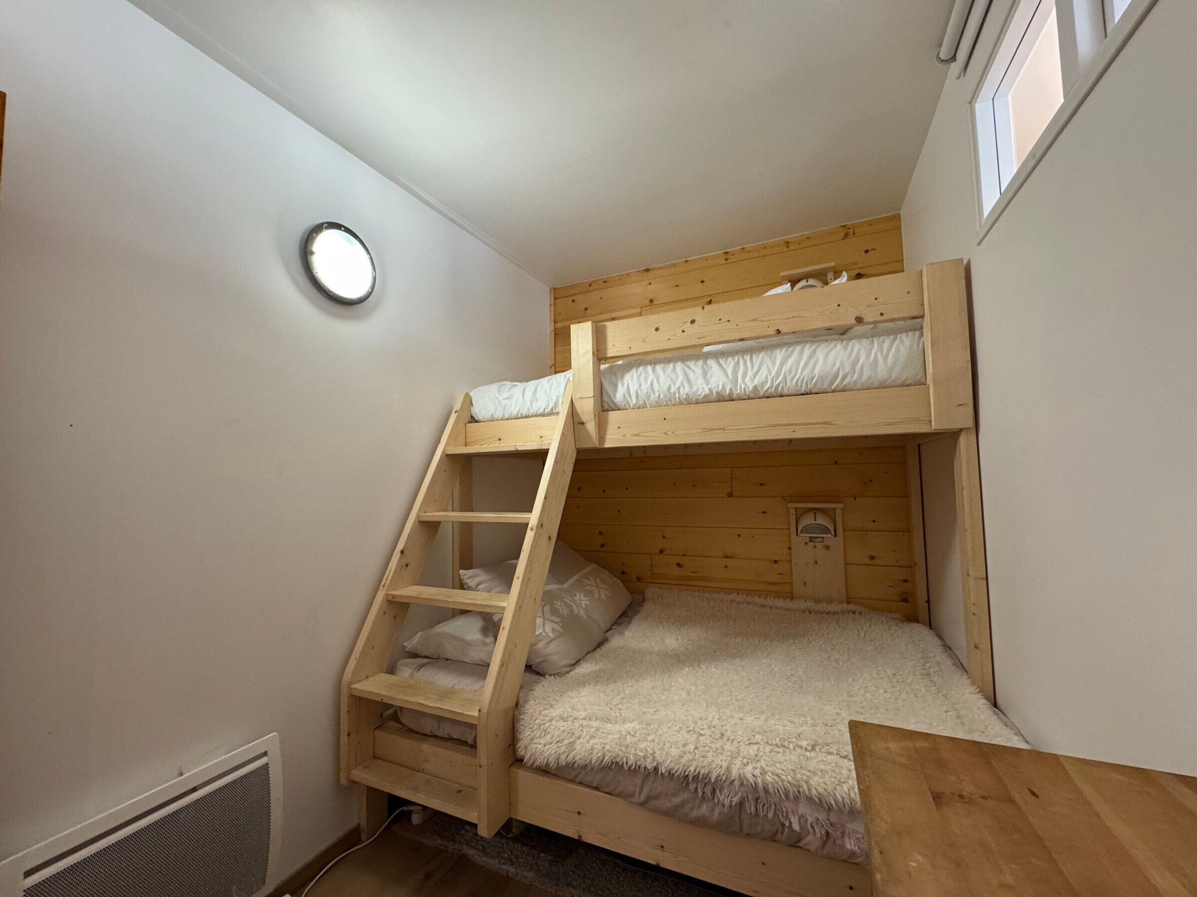A bunk bed room with a ladder, a small heater, and a window.