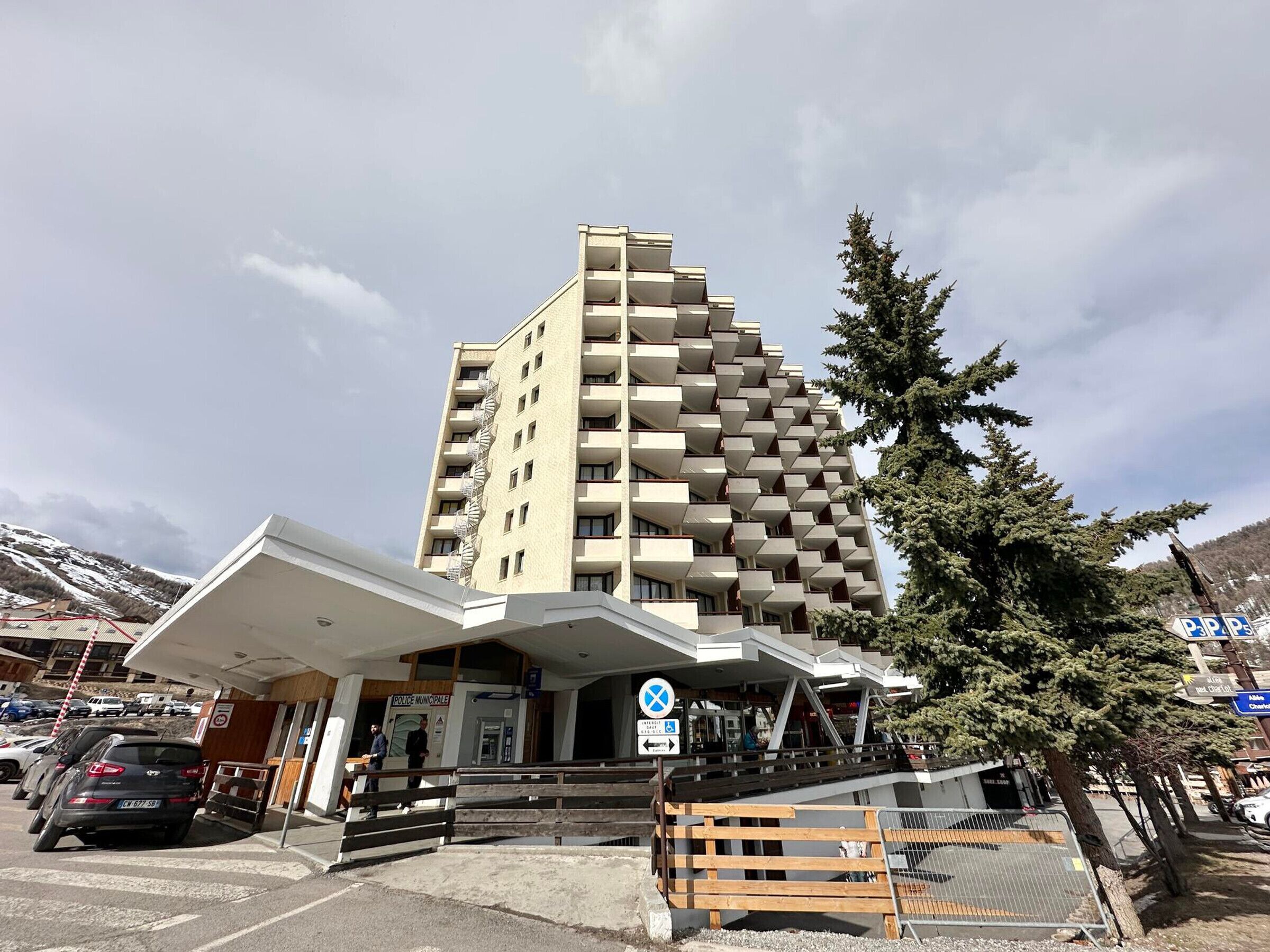 Um hotel de vários andares com design moderno, destacando uma entrada imponente e uma área de estacionamento na frente.