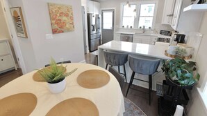A modern kitchen with white cabinets, a stainless steel refrigerator, and a central island with bar stools. - The Brightwood House - Family Living in the Heart of DC! (Washington)
