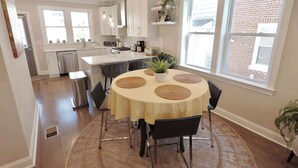 A modern kitchen with white cabinets, a central island, and a dining area with a round table and chairs. - The Brightwood House - Family Living in the Heart of DC! (Washington)