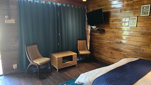 A room with a bed, two chairs, a small table, a TV mounted on the wall, and wooden paneling. - Lemon wood Cottage (Naobaricha)