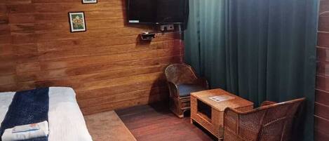 A cozy room with a bed, a television, wicker furniture, and a curtain.