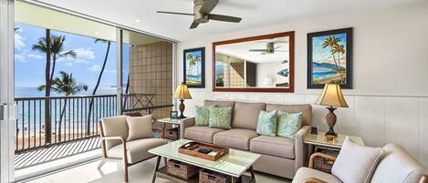 A spacious living area with a balcony overlooking the beach, furnished with a sofa, chairs, and a coffee table.
