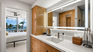 Ein modernes Badezimmer mit Holzausstattung, einem großen Spiegel, einem weißen Waschbecken und Meerblick.