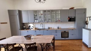 A modern kitchen with grey cabinets, a wooden dining table, and a built-in oven. - L'atelier du Centre D'ax les Thermes (Ax-les-Thermes)