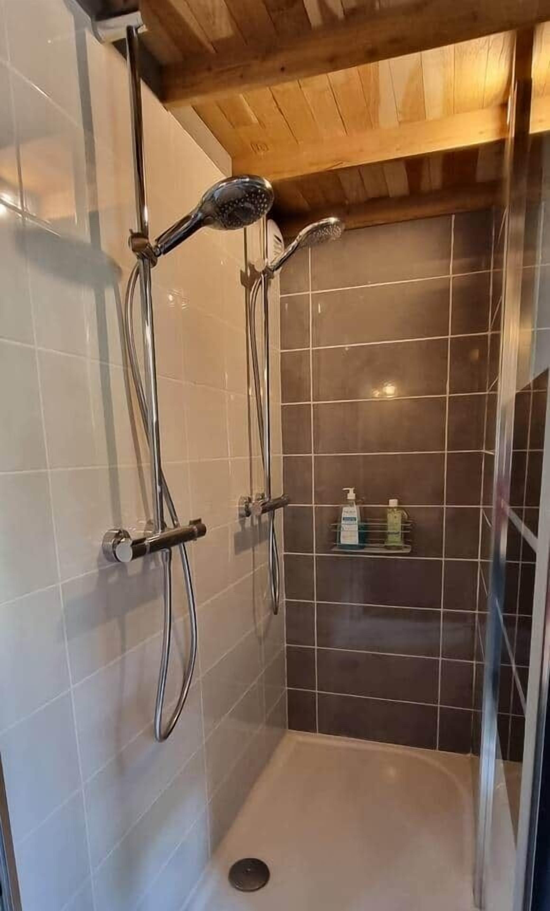 Une douche avec un plafond en bois, des murs carrelés et une étagère où sont rangés les produits de toilette.