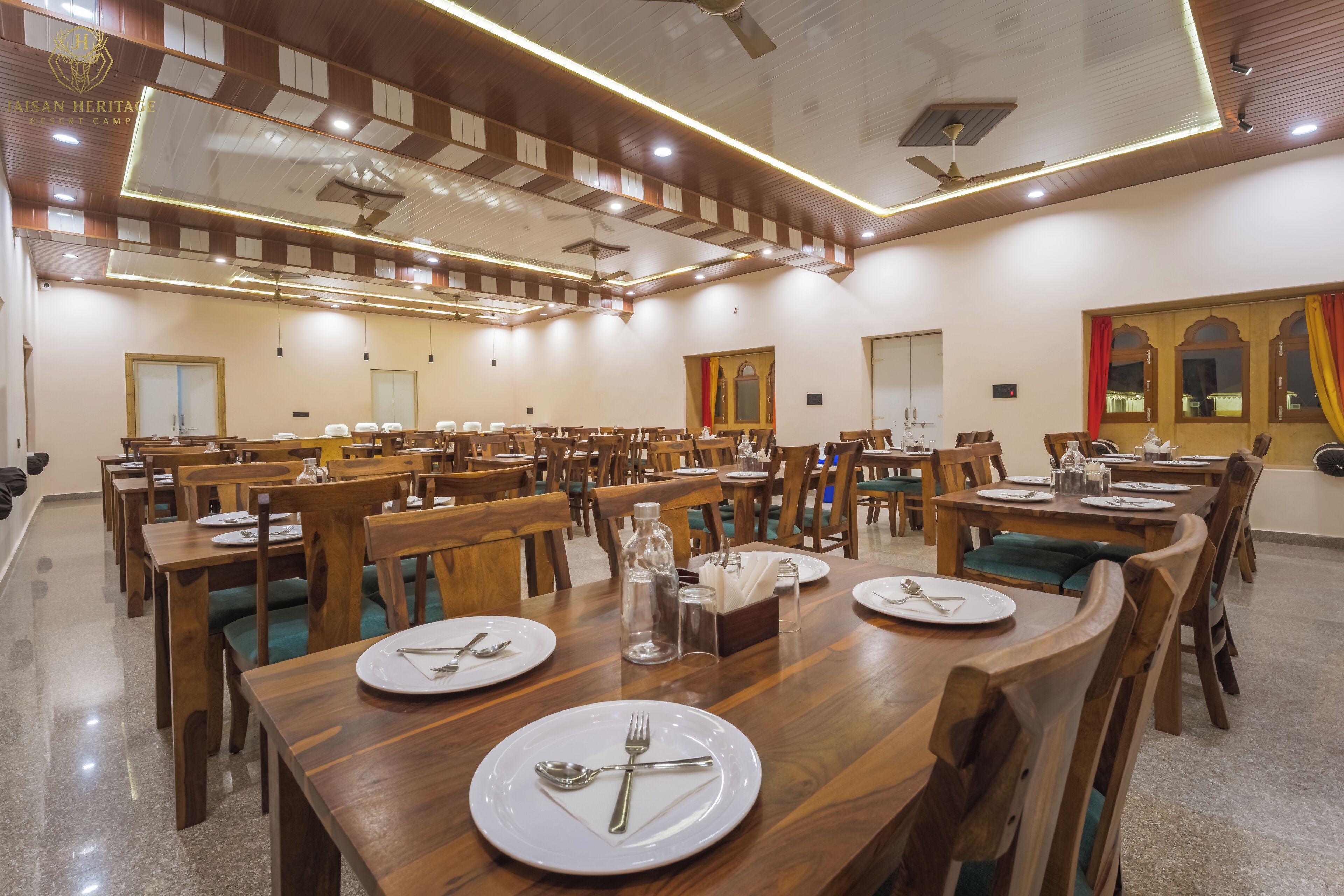 Une vaste salle à manger dotée de nombreuses tables et chaises en bois, ainsi que de la vaisselle, des couverts et des verres.