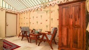 Una habitación con pared estampada, un armario de madera, dos sillas, una mesita con objetos y una alfombra roja.