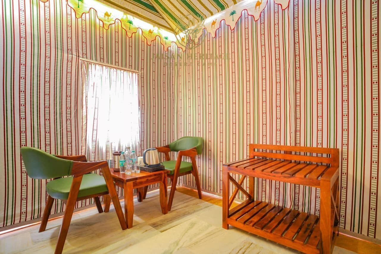 A room with striped wallpaper, a wooden table, two green chairs, and a wooden bench.