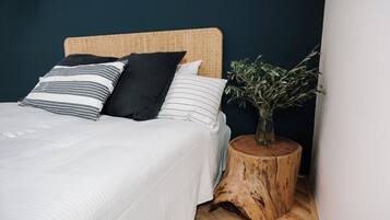 Ein Bett mit einem gewobenen Kopfteil, ein Nachttisch mit einem Holzstumpf und eine Vase mit Grünpflanzen.