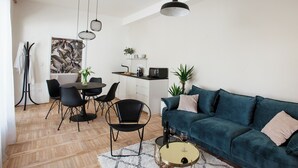 Een moderne woonkamer met een donkergroene bank, zwarte stoelen, een eettafel en een keuken in de achtergrond.