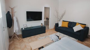 Een moderne woonkamer met een donkere bank, houten vloer en een aan de muur bevestigde televisie.