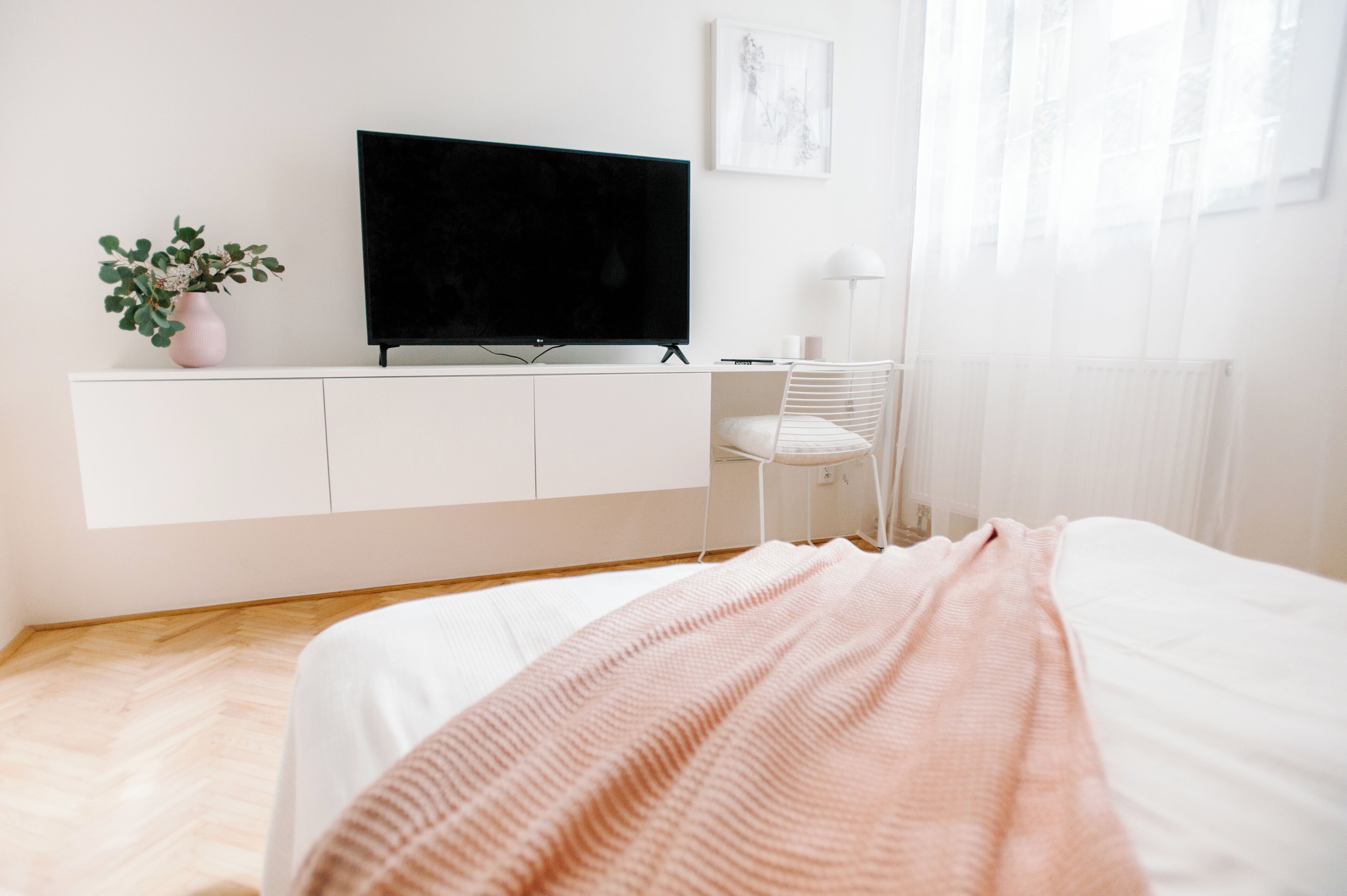 Un dormitorio con una cama, un televisor sobre un mueble blanco, una silla y una planta en maceta.