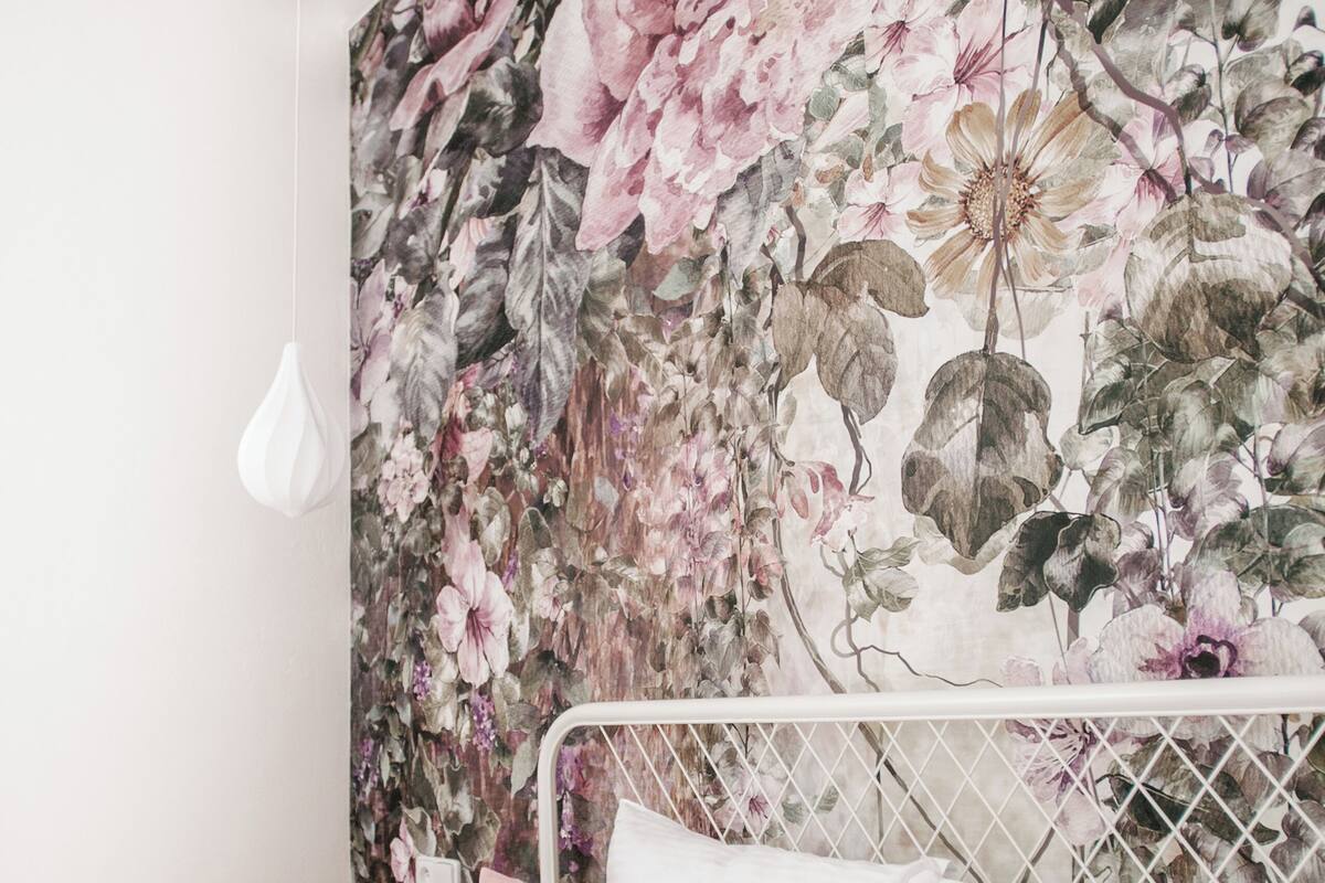 A bedroom with a floral wallpaper, a white metal headboard, and a pink pillow.