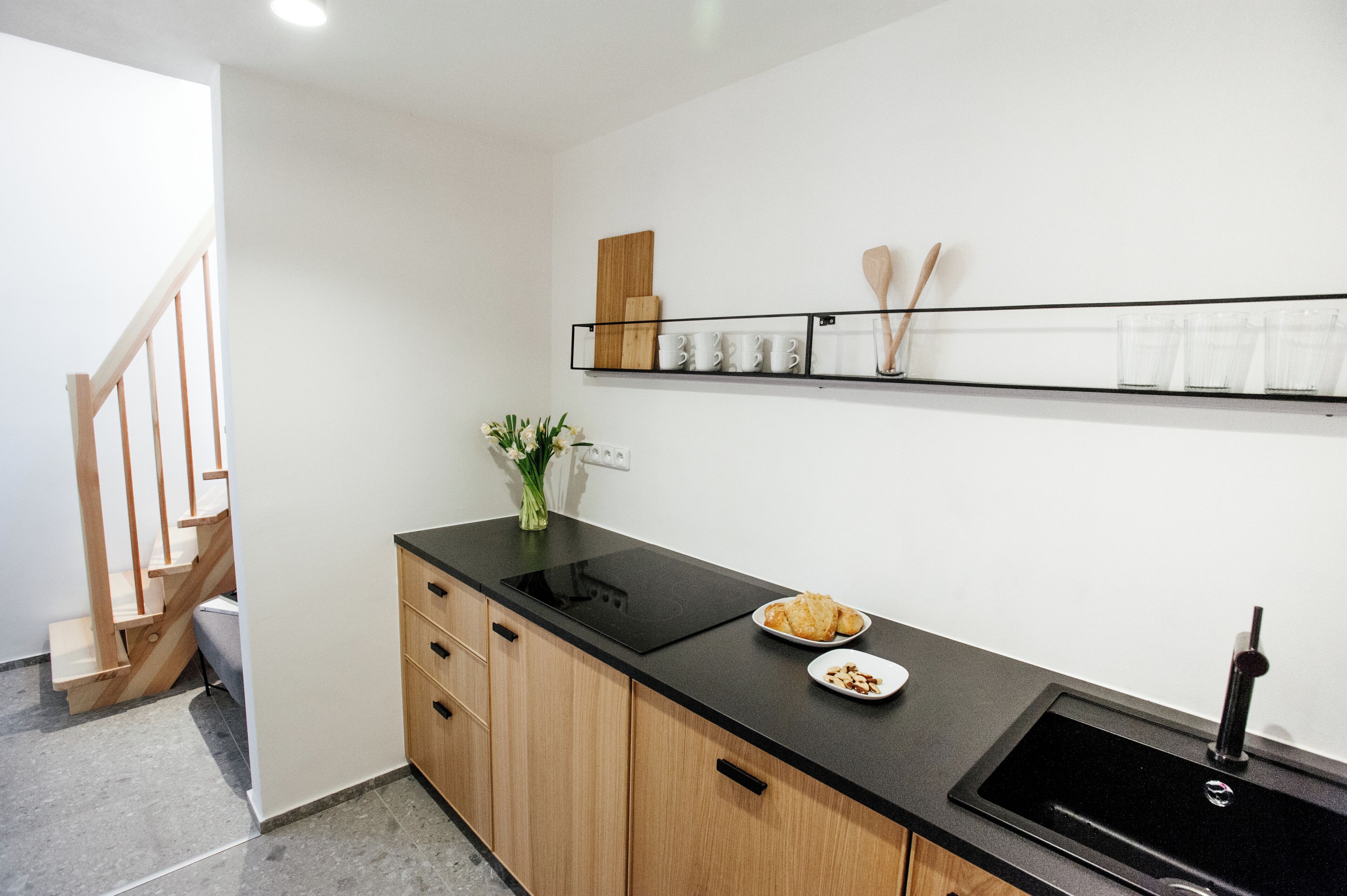 Een moderne keuken met een zwart aanrecht, houten kastjes, een zwarte spoelbak en een houten trap.