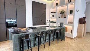 A modern kitchen with a central island, bar stools, and built-in shelves. - Palais Oyena (Marrakech)