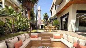 An outdoor seating area with a glass coffee table, cushioned sofas, and a dining table with chairs. - Palais Oyena (Marrakech)