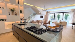 A modern kitchen with a central island, built-in shelves, and a staircase leading to an upper level. - Palais Oyena (Marrakech)