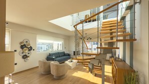 A spacious living room with a modern staircase, a blue sofa, and a coffee table.