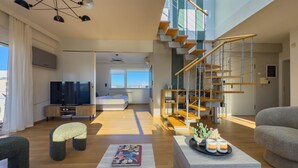 A modern living room with a large TV, comfortable seating, a staircase, and a view of the city.