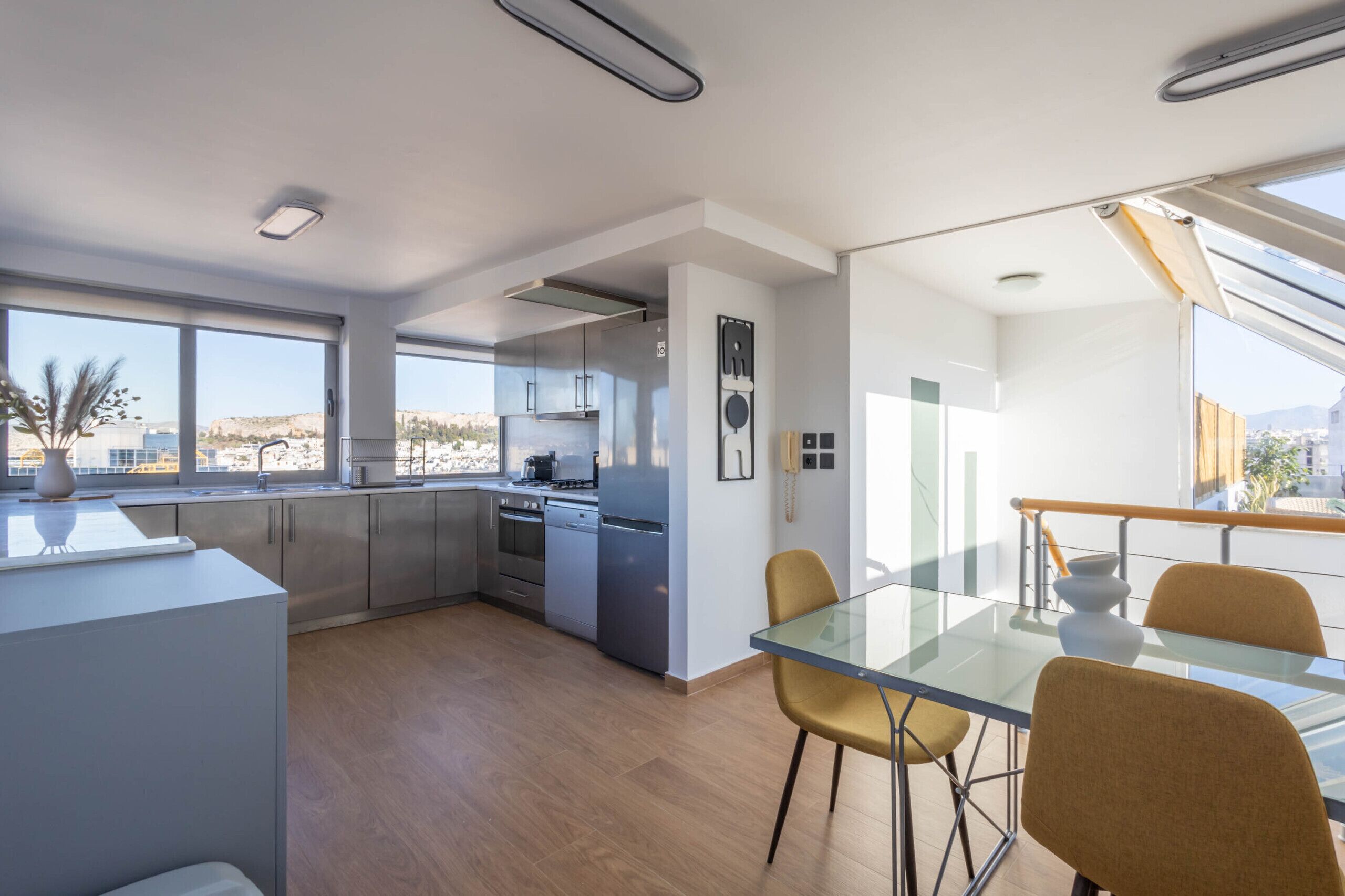 Een moderne keuken met roestvrijstalen apparatuur, een eetgedeelte met een glazen tafel en stoelen, en grote ramen met uitzicht op de stad.