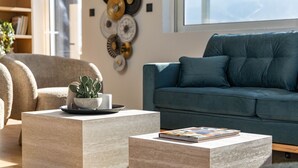 A modern living room with two square coffee tables, a blue sofa, and a bookshelf with books and decorative items.