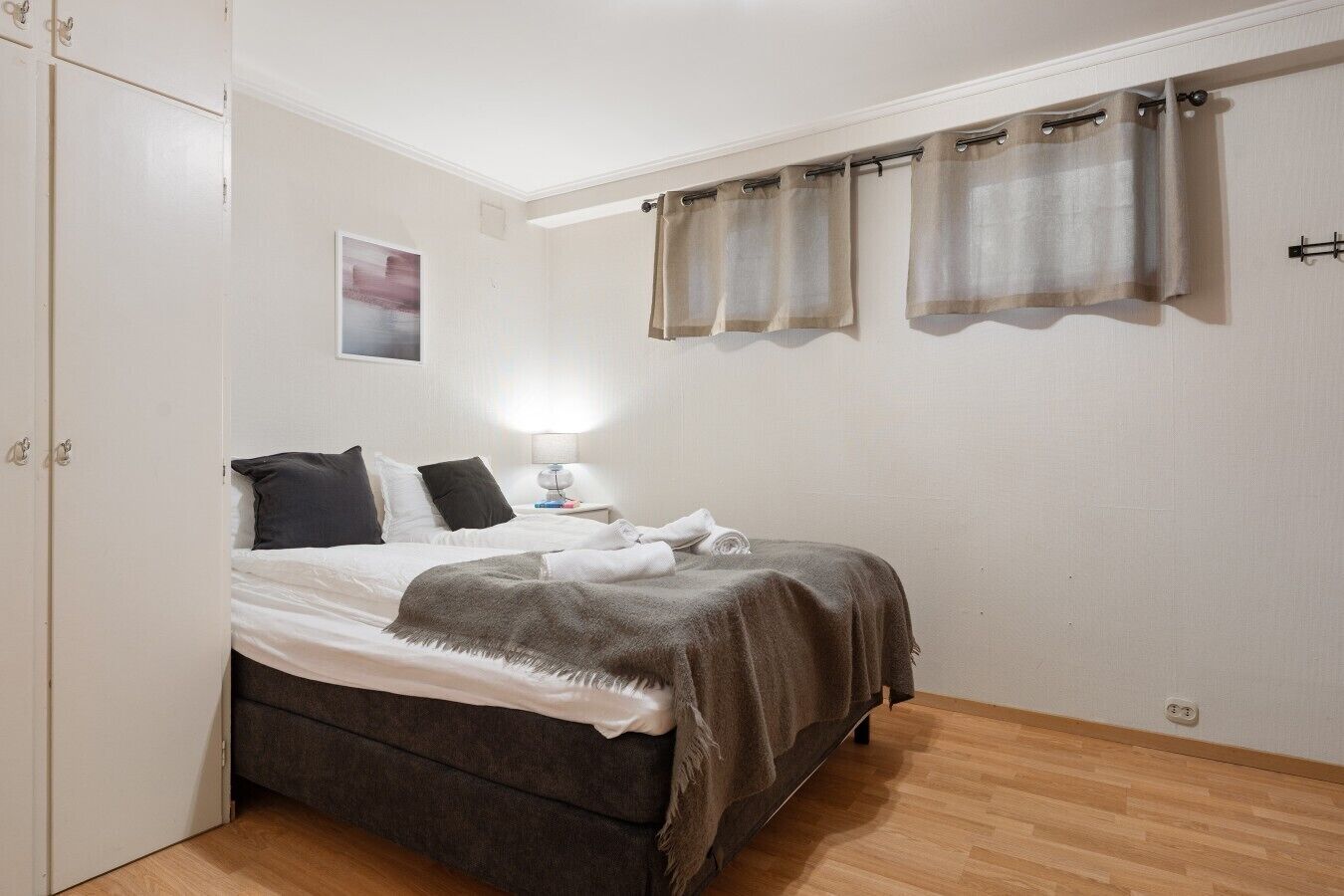 Een slaapkamer met een bed, nachtkastje, lamp en een kledingkast.