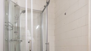 Une douche fermée par des parois de verre, dotée d’une porte incurvée, de murs recouverts de carreaux blancs et d’un sol carrelé.