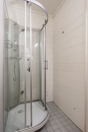 A glass-enclosed shower with a curved door, white tiled walls, and a tiled floor. - Røstbakken Downtown Apartments (Tromsø)