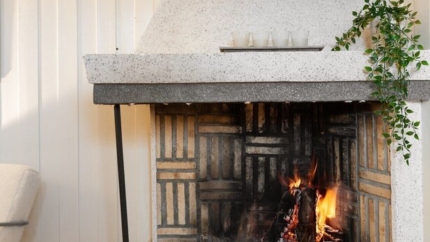 Une cheminée avec un motif en pierre mouchetée, un feu qui crépite à l’intérieur, et une plante sur la droite.