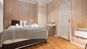 Une chambre à coucher comprenant un lit, une table de chevet, une armoire et une salle de bain avec un lavabo, ainsi qu’une porte.