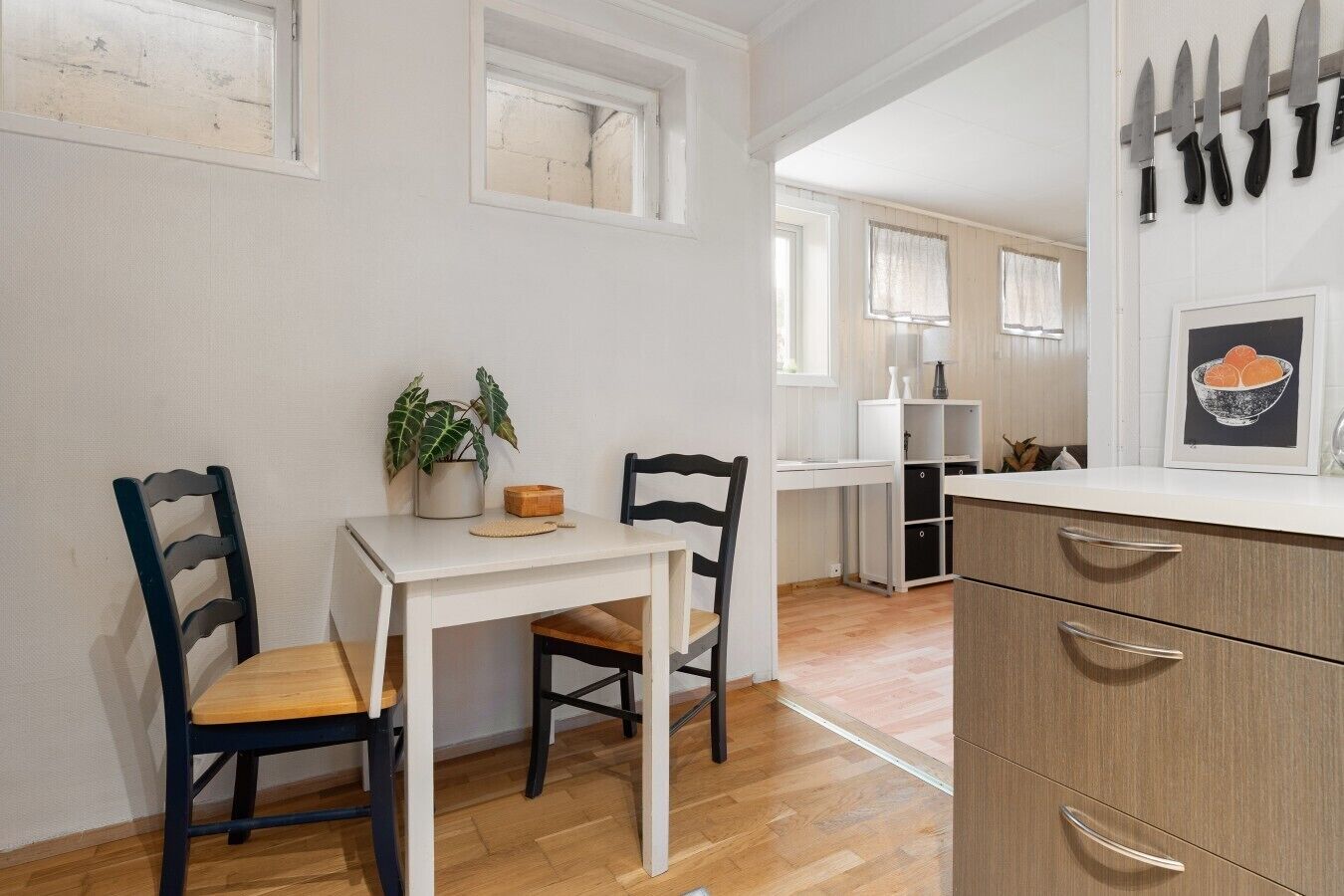 A kitchen with a white table, two chairs, a potted plant, and a cabinet with drawers.