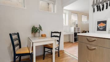 A kitchen with a white table, two chairs, a potted plant, and a cabinet with drawers.