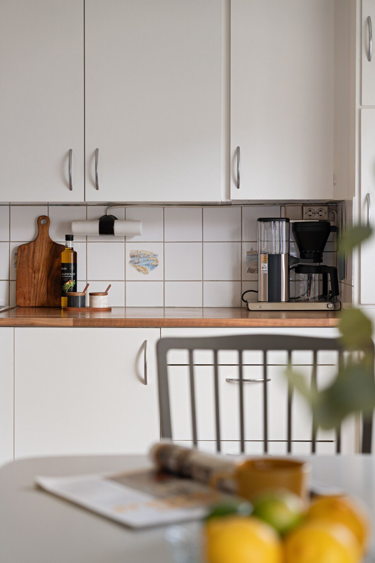 Eine Küche mit weißen Schränken, einem HolzbCutting Board, einer Olivenölflasche und einer Kaffeemaschine.