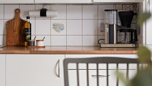 Et køkken med hvide skabe, en træskærebræt, en flaske olivenolie og en kaffemaskine.