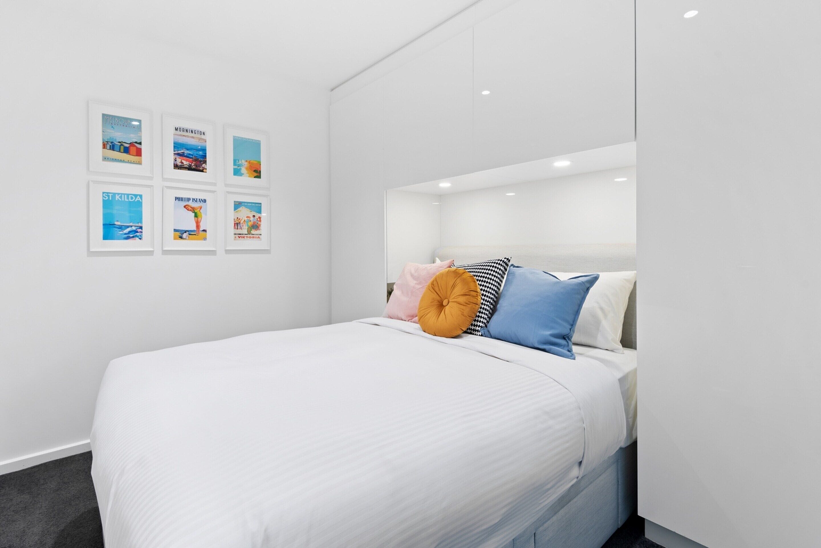 A modern bedroom with a large bed, white walls, and framed pictures on the wall.