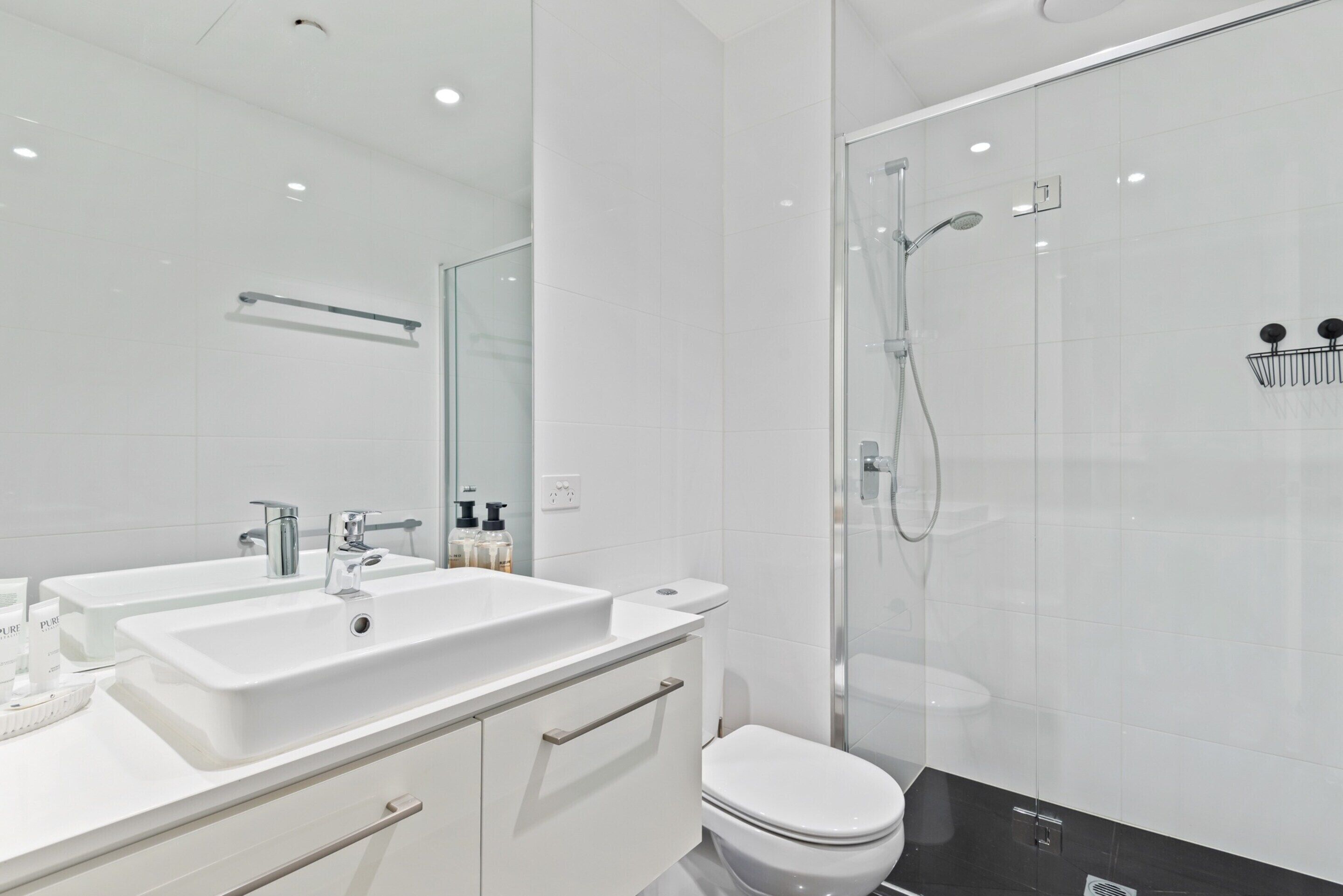 Ein modernes Badezimmer mit zwei Waschbecken, einer Toilette und einer Dusche mit Glastrennwand.
