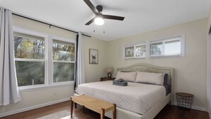 A bedroom with a bed, a ceiling fan, a window with curtains, a bedside table, and a bench. - CozyCottage_Sleeps8_Near Plaza and KU_and Shopping (Mission)