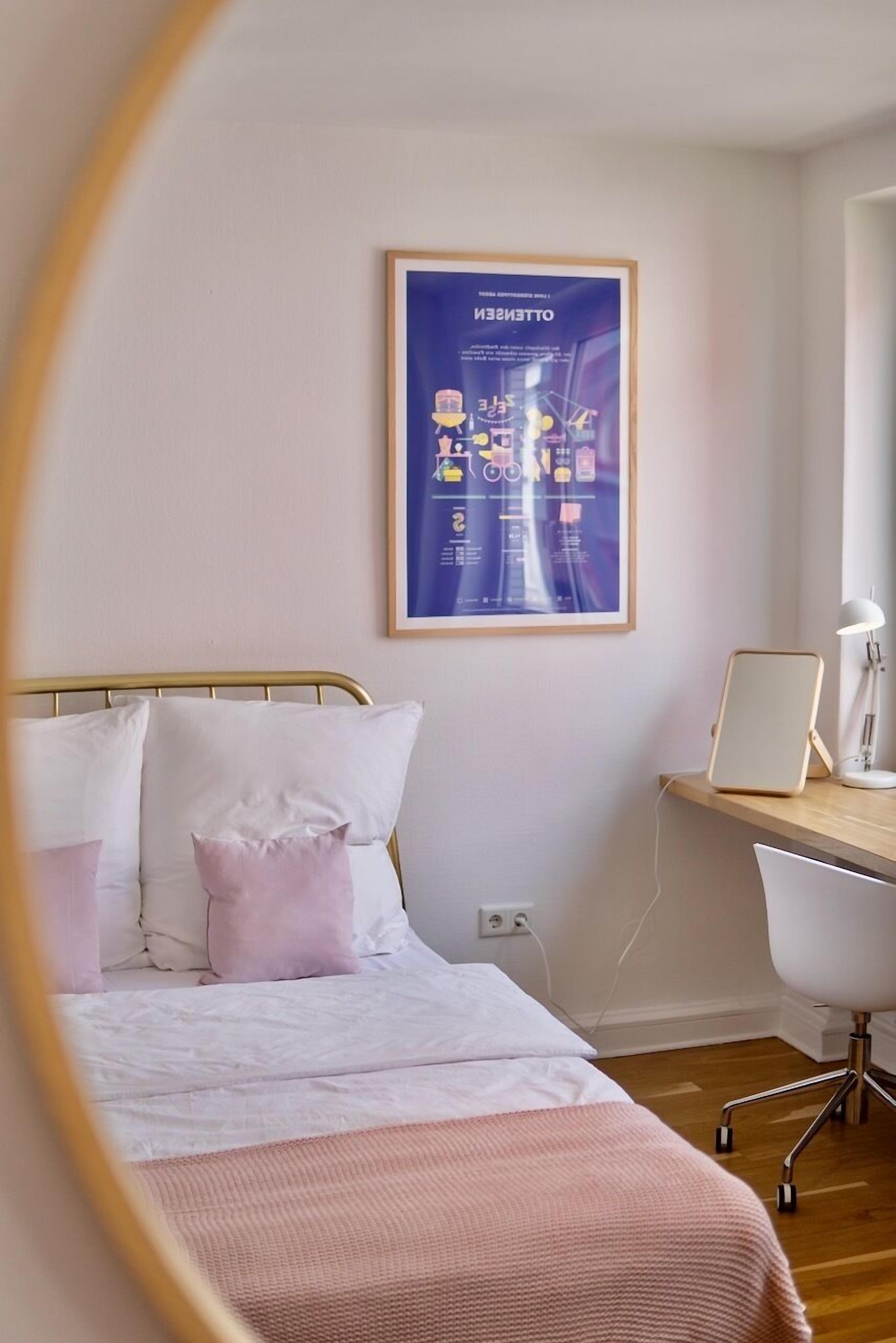 A bedroom with a bed, a desk, and a chair. There is a poster on the wall and a lamp on the desk.